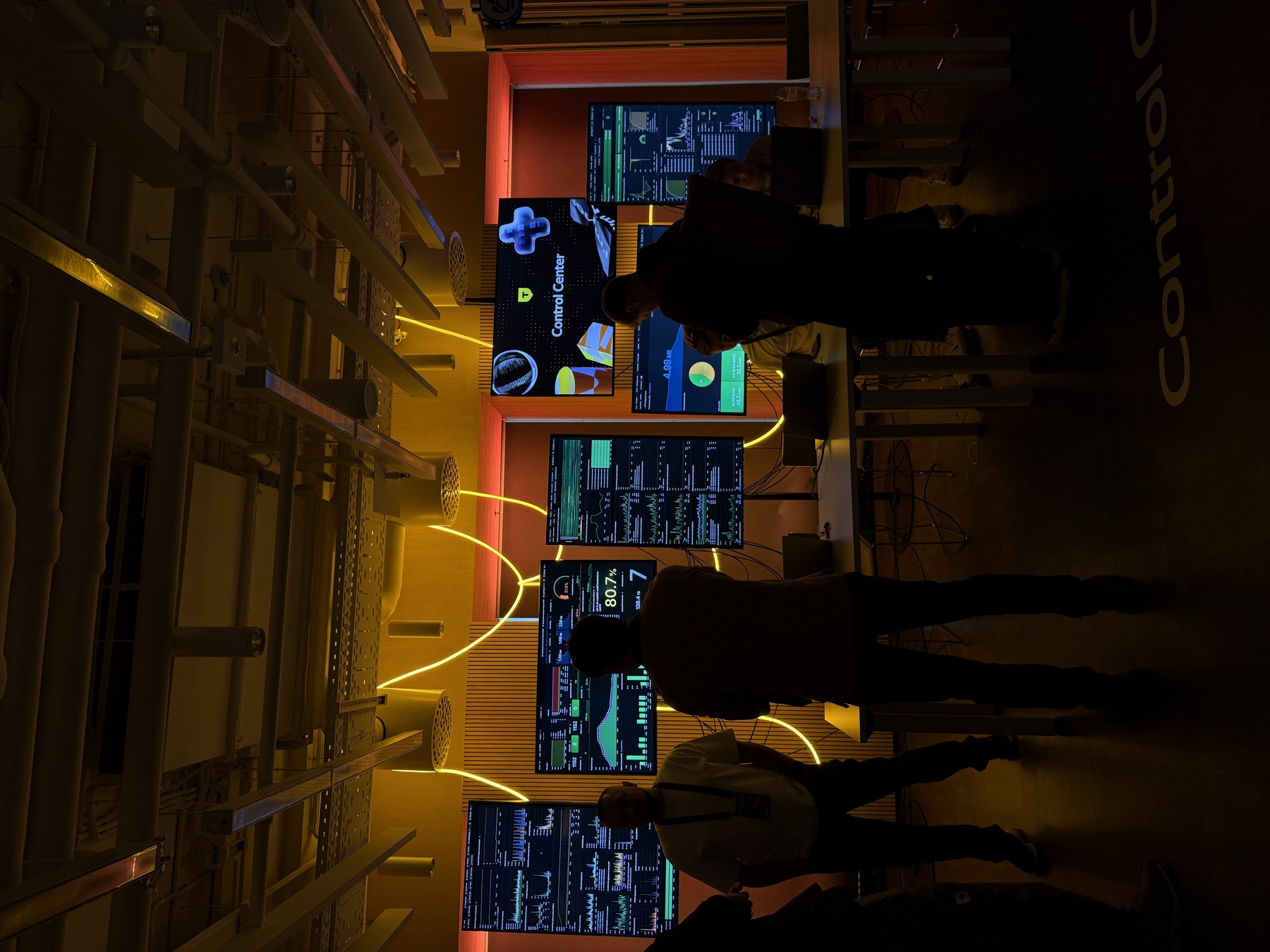 A control room with a row of monitoring dashboards on the wall
