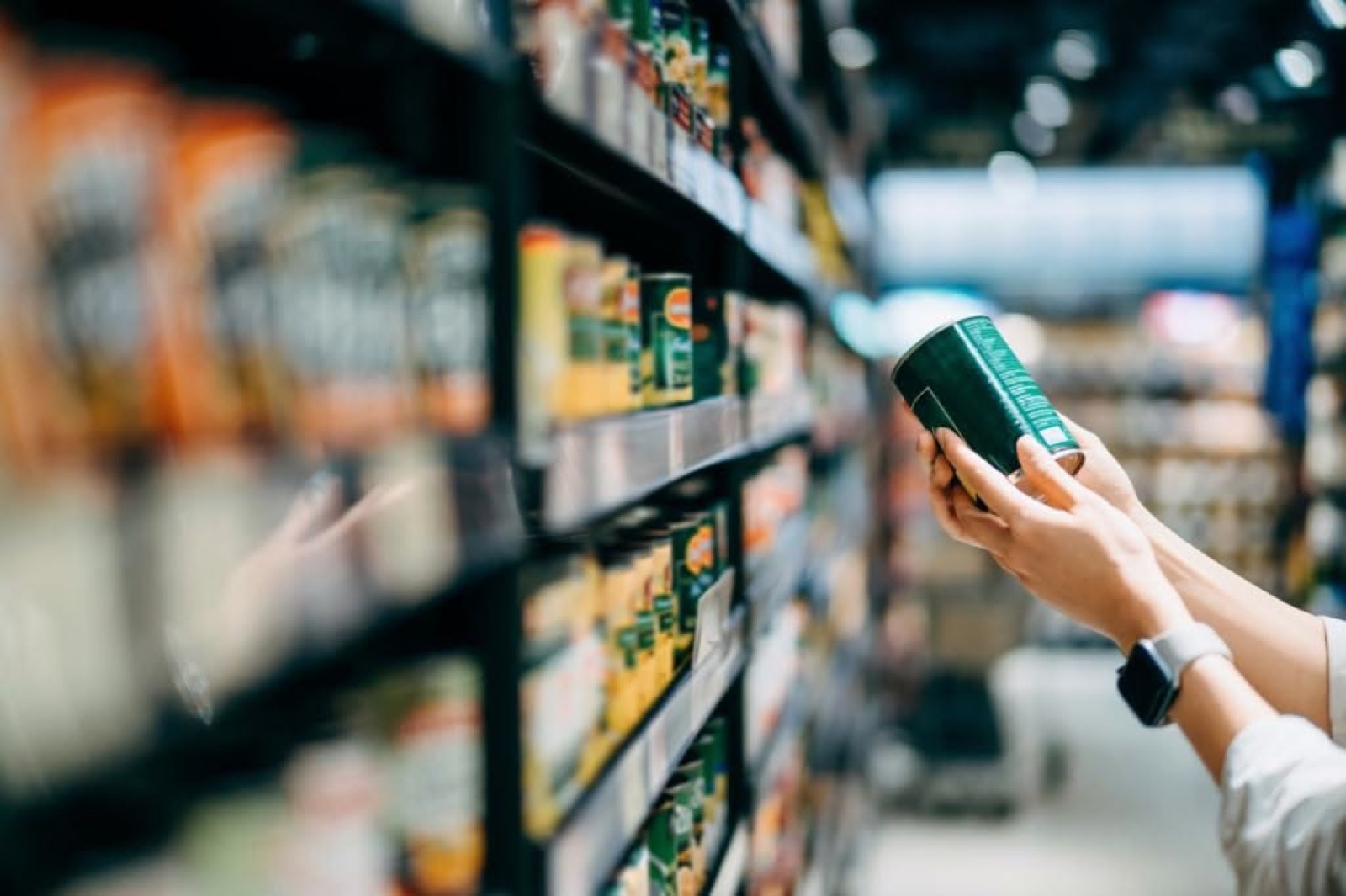 A shopper reading the label on a tin in a supermarket aisle