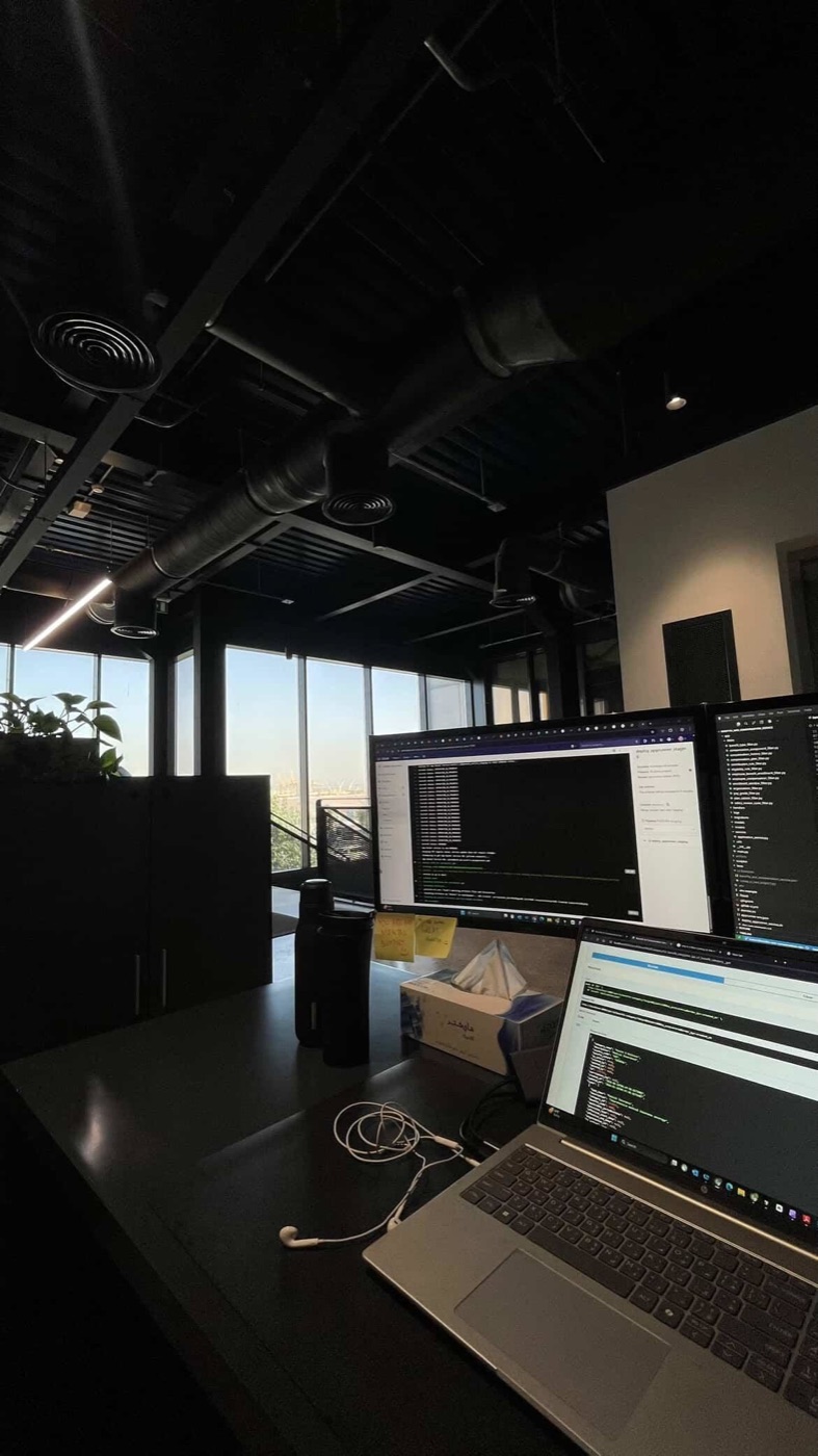 A desk with two screens of code and a laptop, in a quiet office